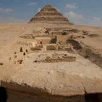 A view of the excavation site. In the foreground is the edge of the Dry Moat; in the background is the Step Pyramid; between them are the remains of the tombs of the Lower Necropolis (on the right) and the pits where the burials of the Upper Necropolis were located.